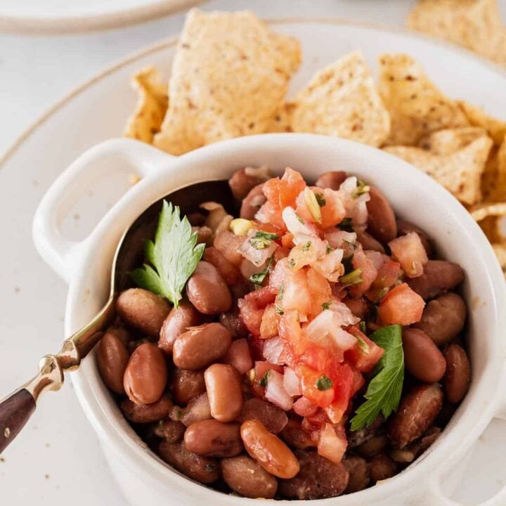 Pinto beans with pico de gallo in white bowl and chips on side.