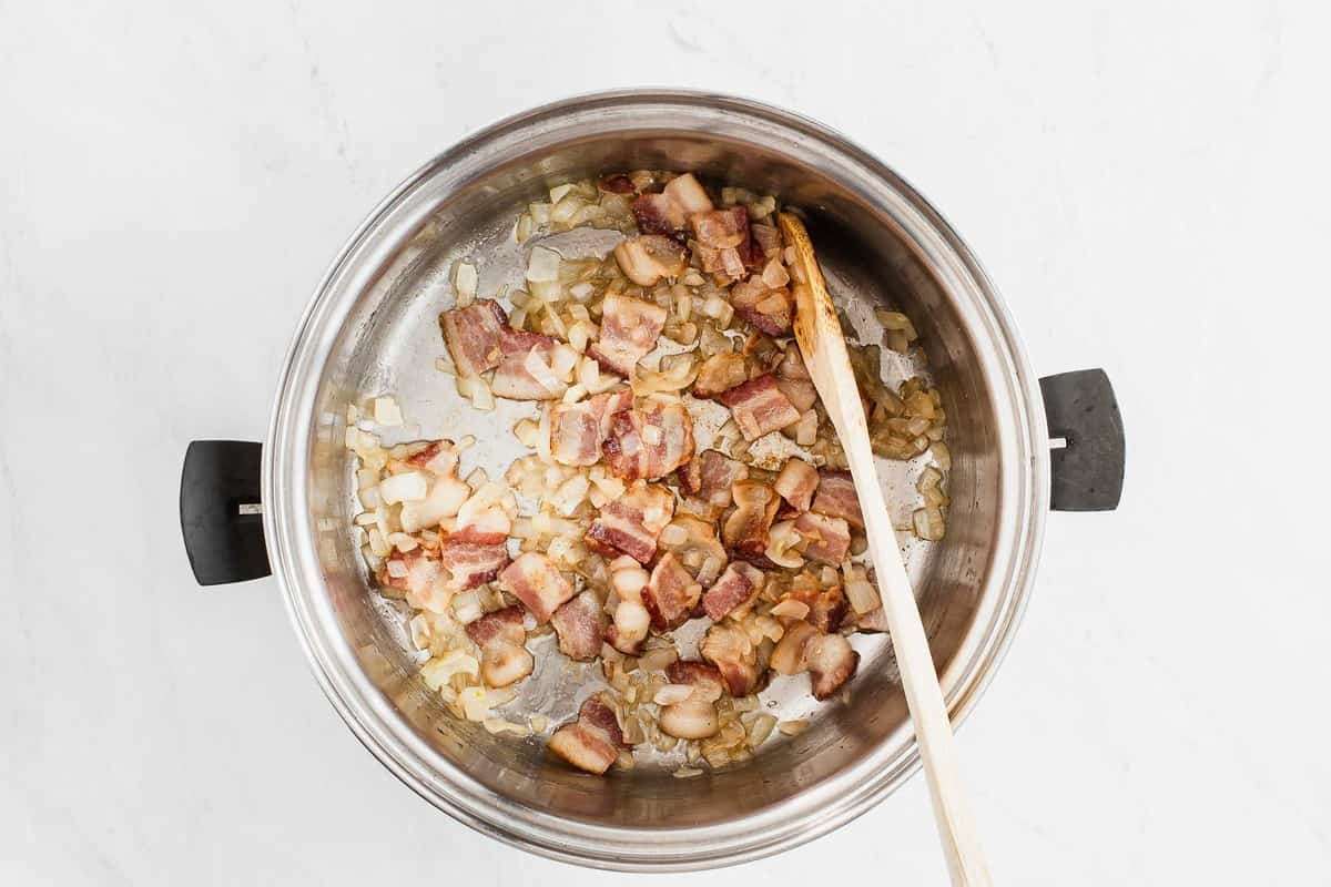 Bacon and onions cooking in a large silver pot.