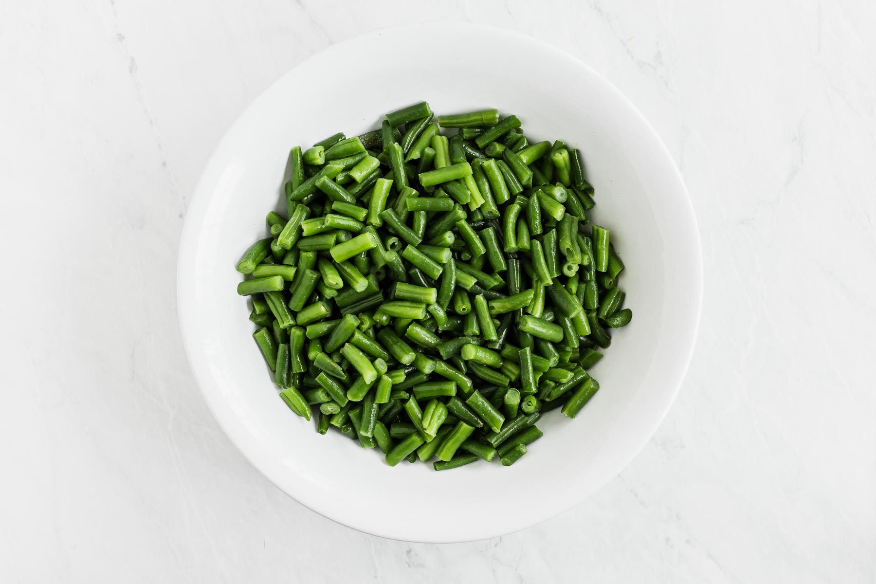 Raw cut green beans in a white bowl.