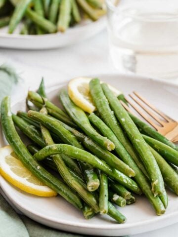 Sauteed green beans on a plate with lemon slices.