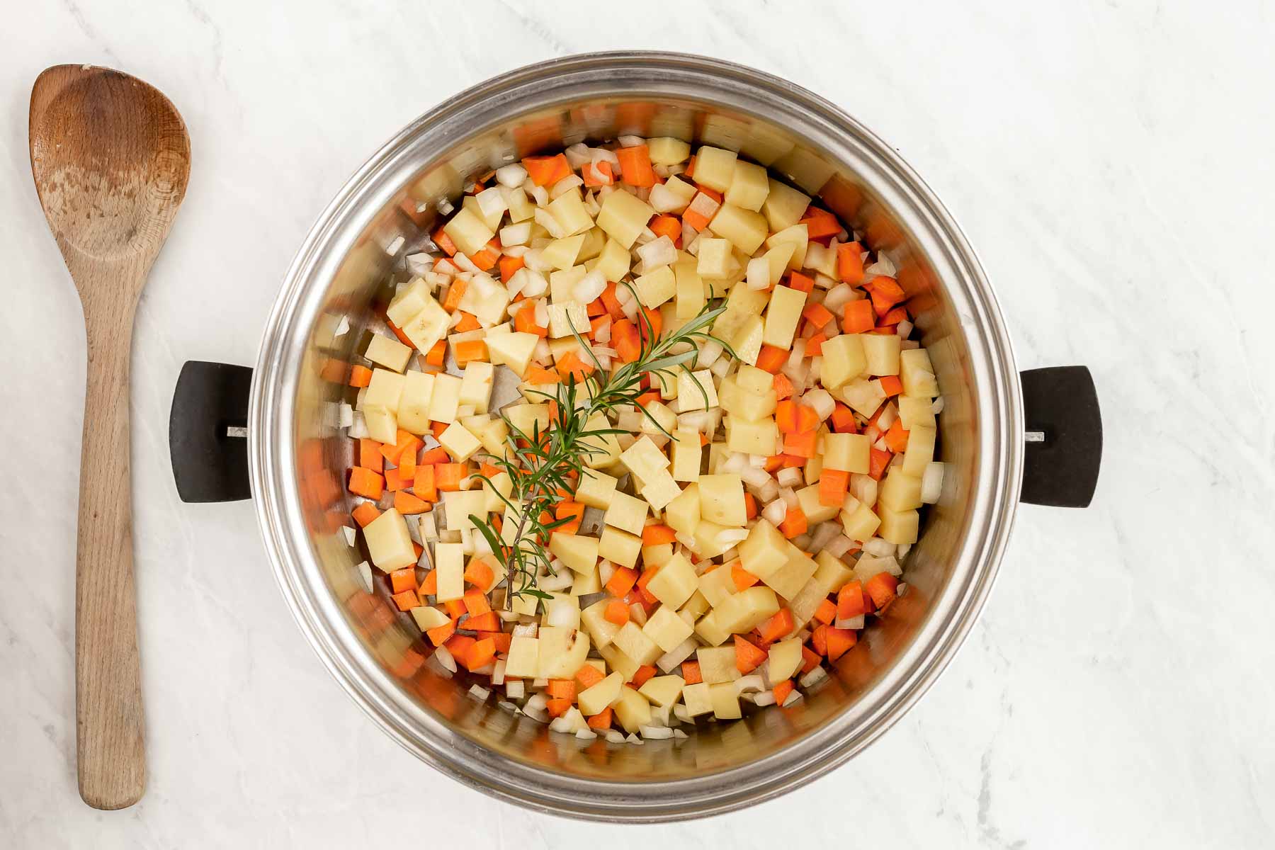 Onions, carrot and potato with a rosemary sprig sautéing in a soup pot.