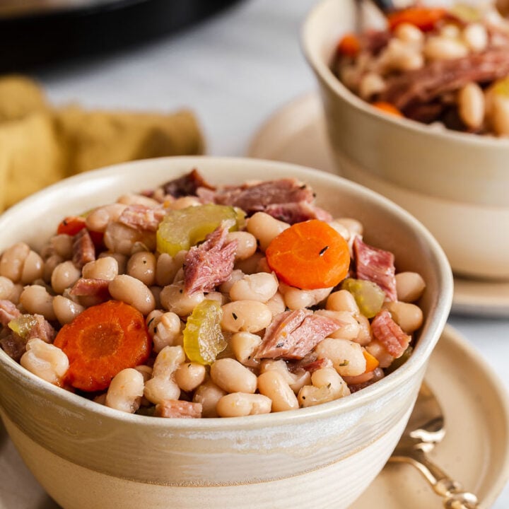 Cream bowl of white beans, carrot coins, and ham pieces.
