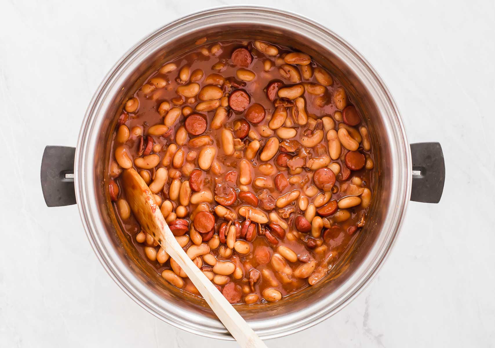 Cooked pork and beans in a pot with wooden spoon.