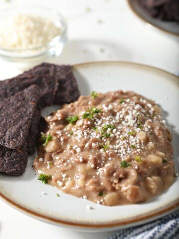 Refried beans on plate with blue corn tortilla chips.