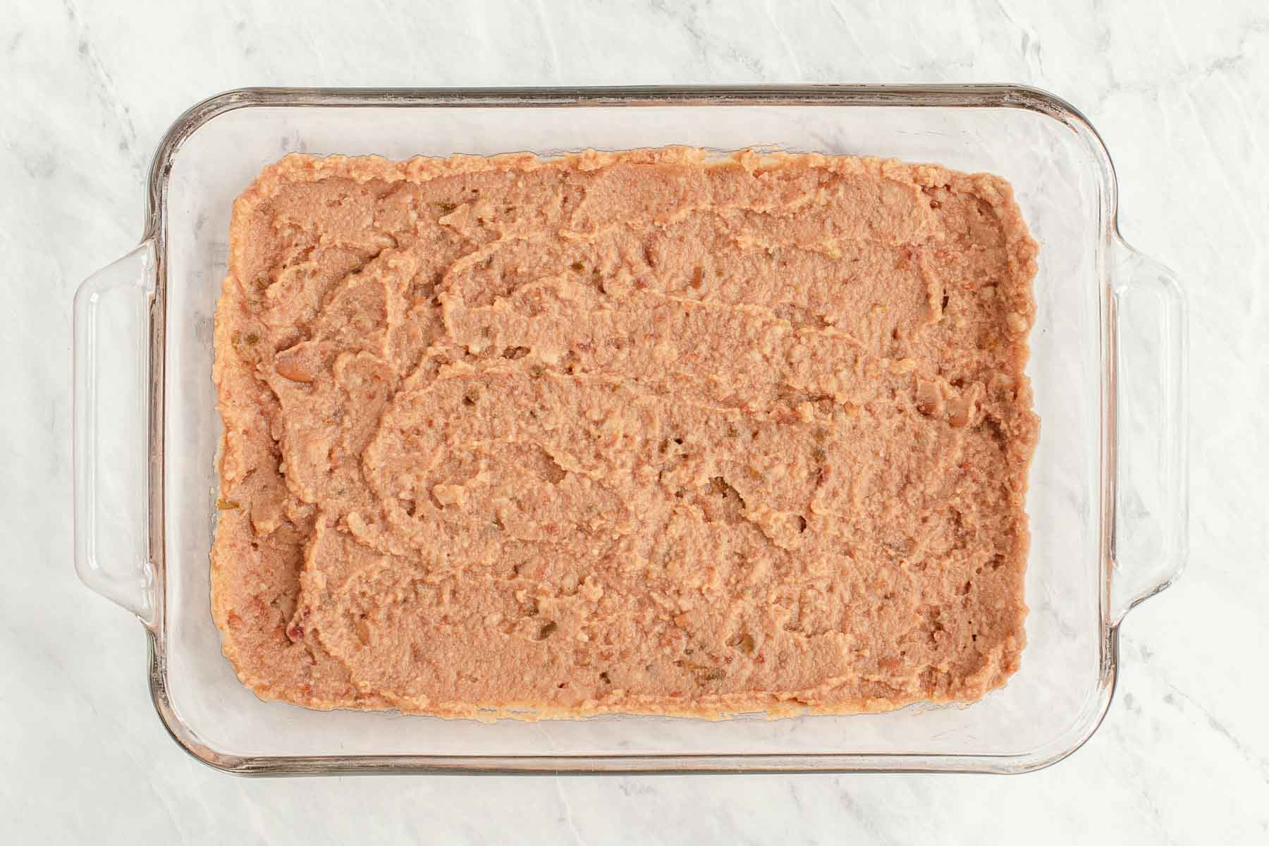 Refried beans spread in a casserole dish.