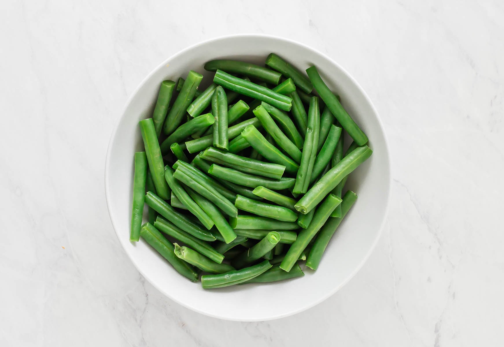 Freshly steamed green beans in white bowl.