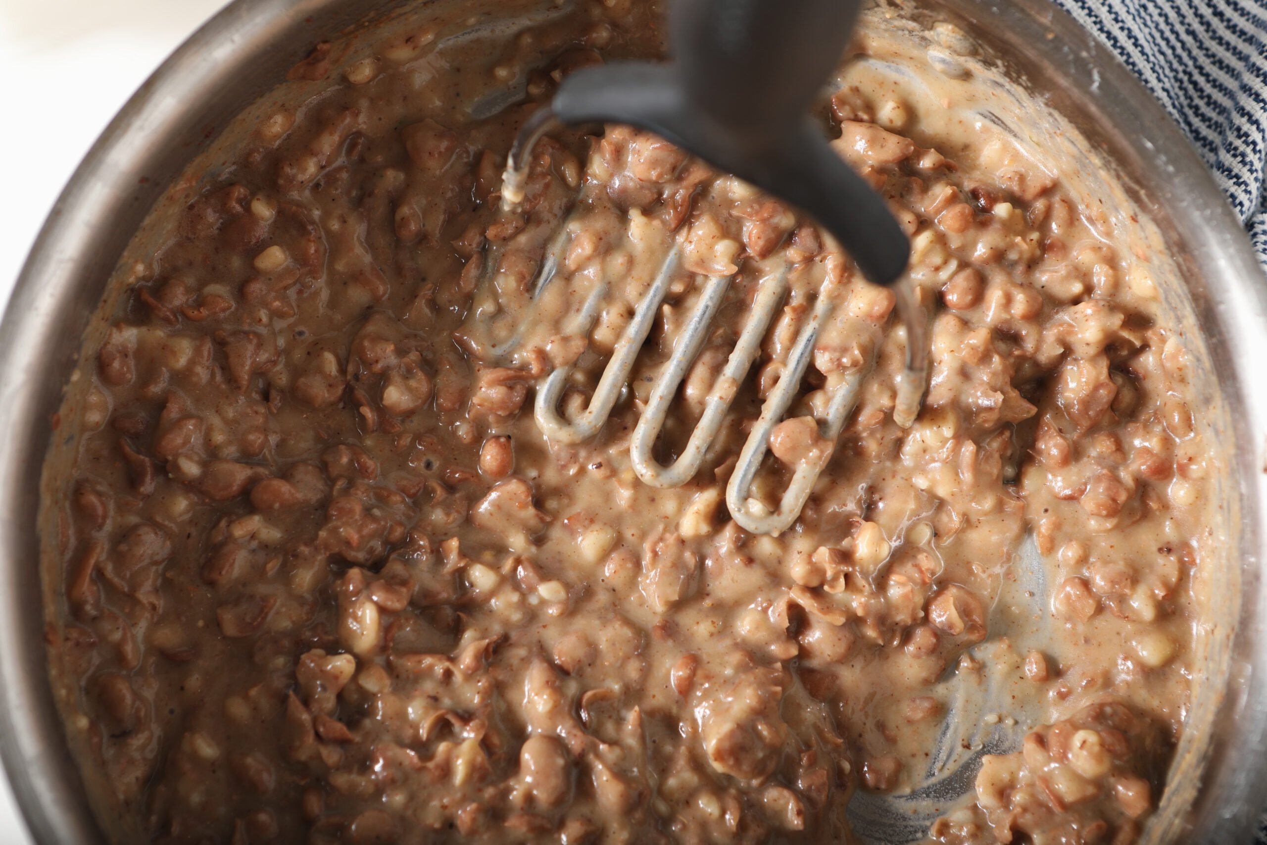 Smashed refried beans in a pot with potato masher.