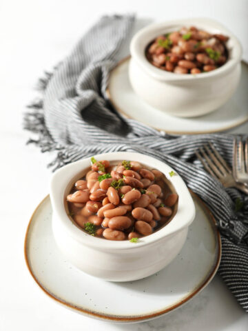 Two white bowls of pinto beans garnished with cilantro.
