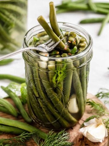 Pickled green beans in jar with fork removing two beans.