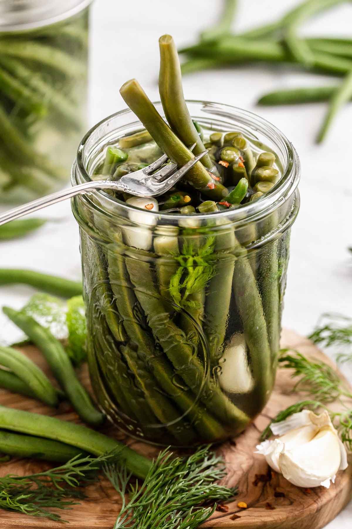Pickled green beans in jar with fork removing two beans.