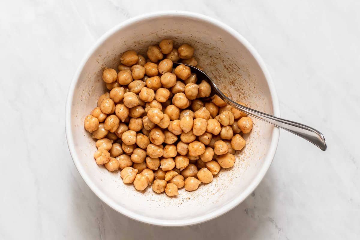 Chickpeas tossed in bowl with oil and spices.