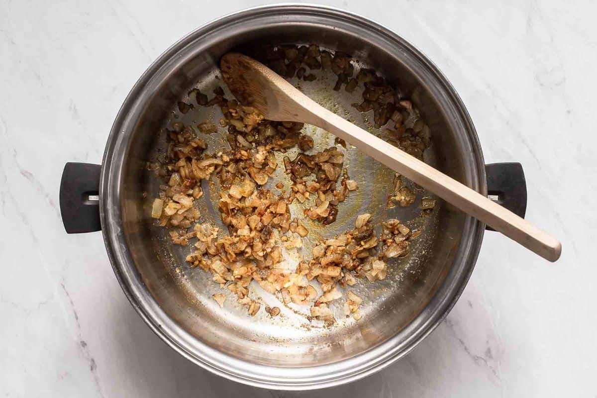 Spices and onions cooking in a pot with wooden spoon.