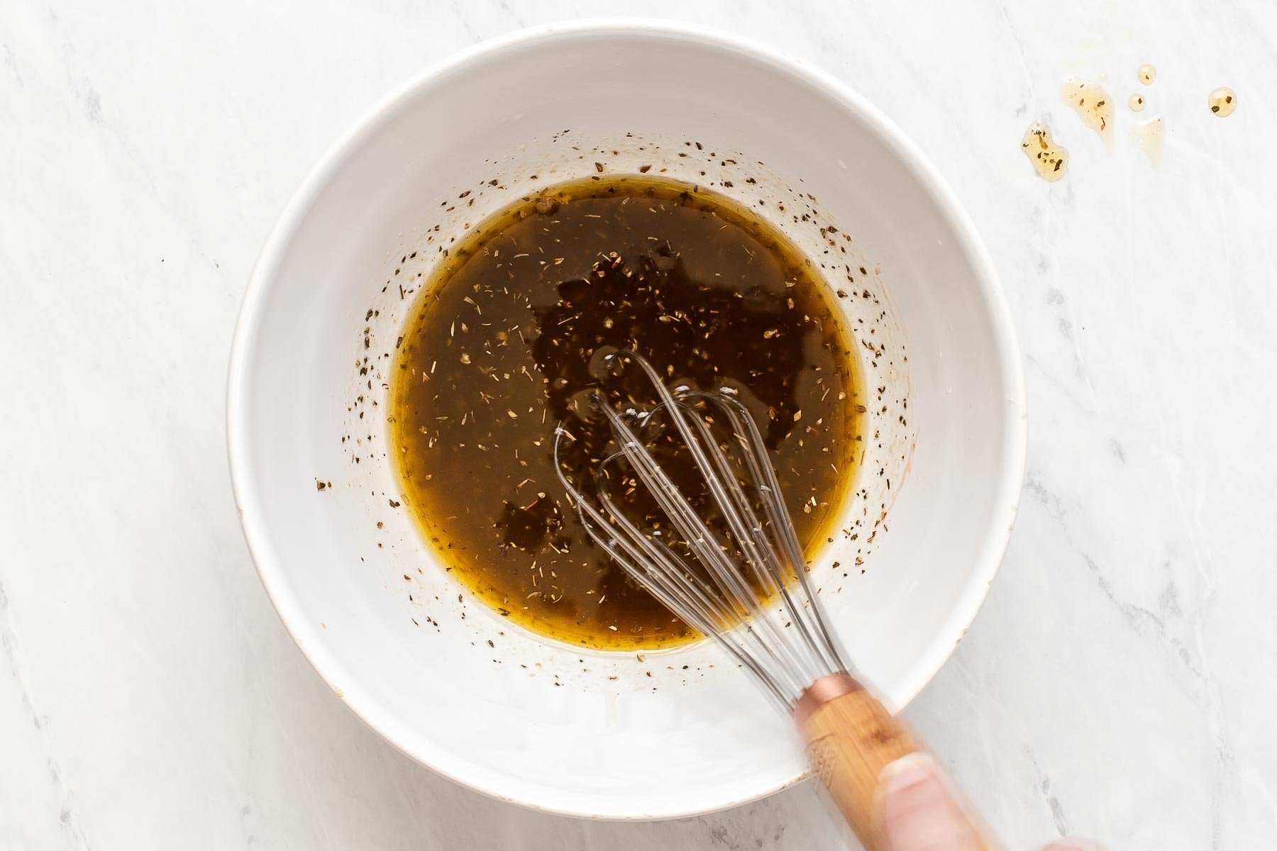 Salad dressing in the bottom of a white bowl with whisk.