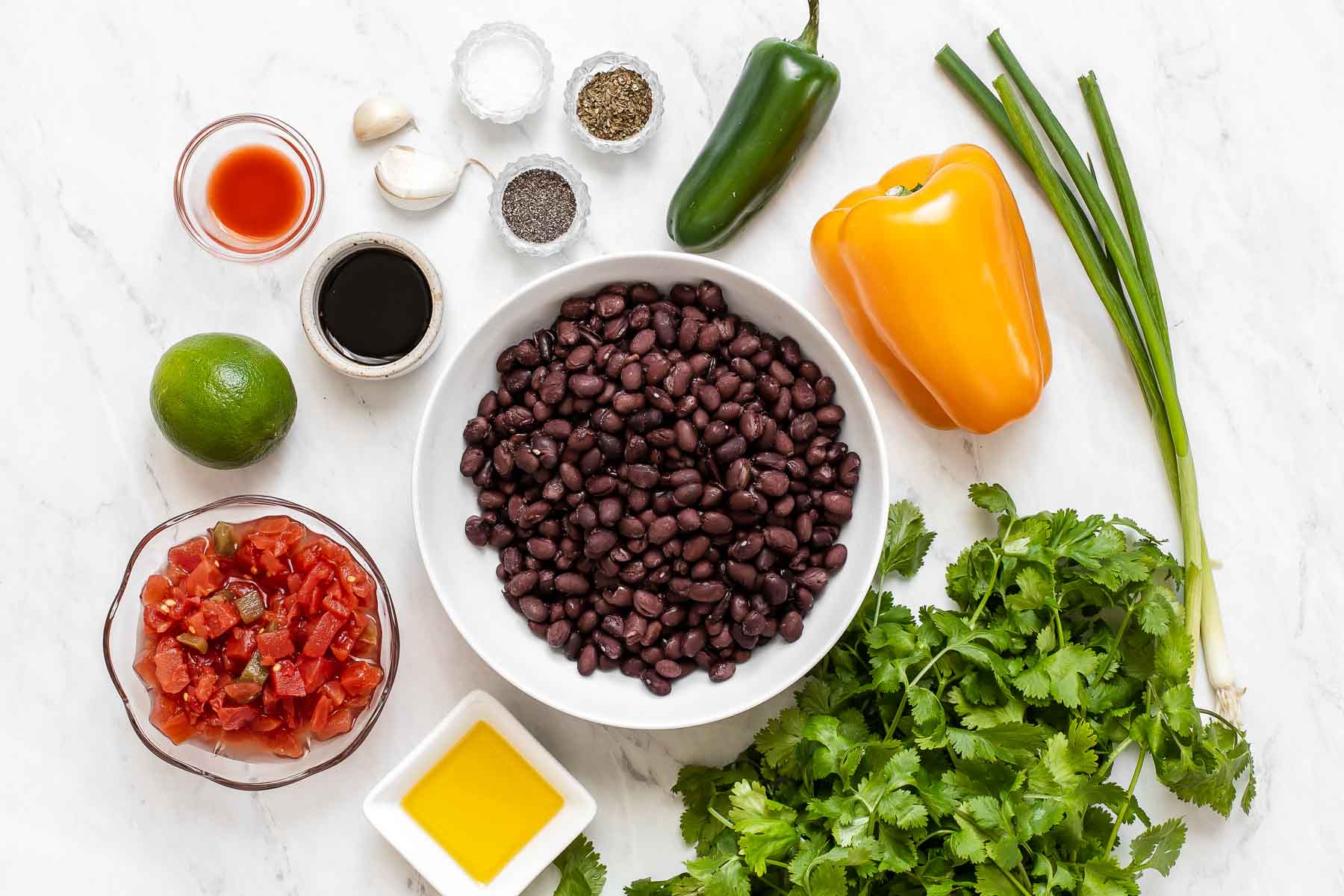 Ingredients for black bean salad in bowls on white surface.
