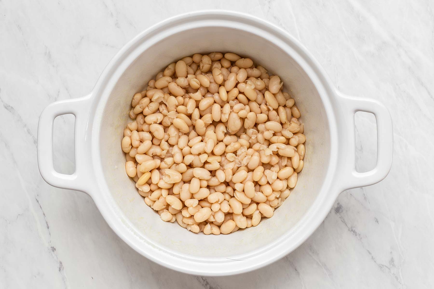 Freshly cooked white beans in round white casserole dish.