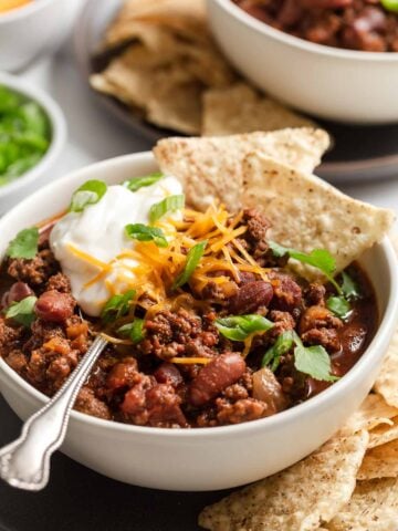 Bowl of chili with beans topped with chips, sour ream and cilantro.