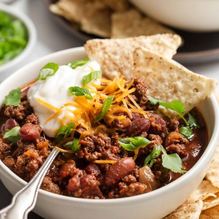 Bowl of chili with beans topped with chips, sour ream and cilantro.