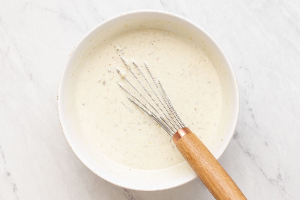 White sauce in bowl with whisk.