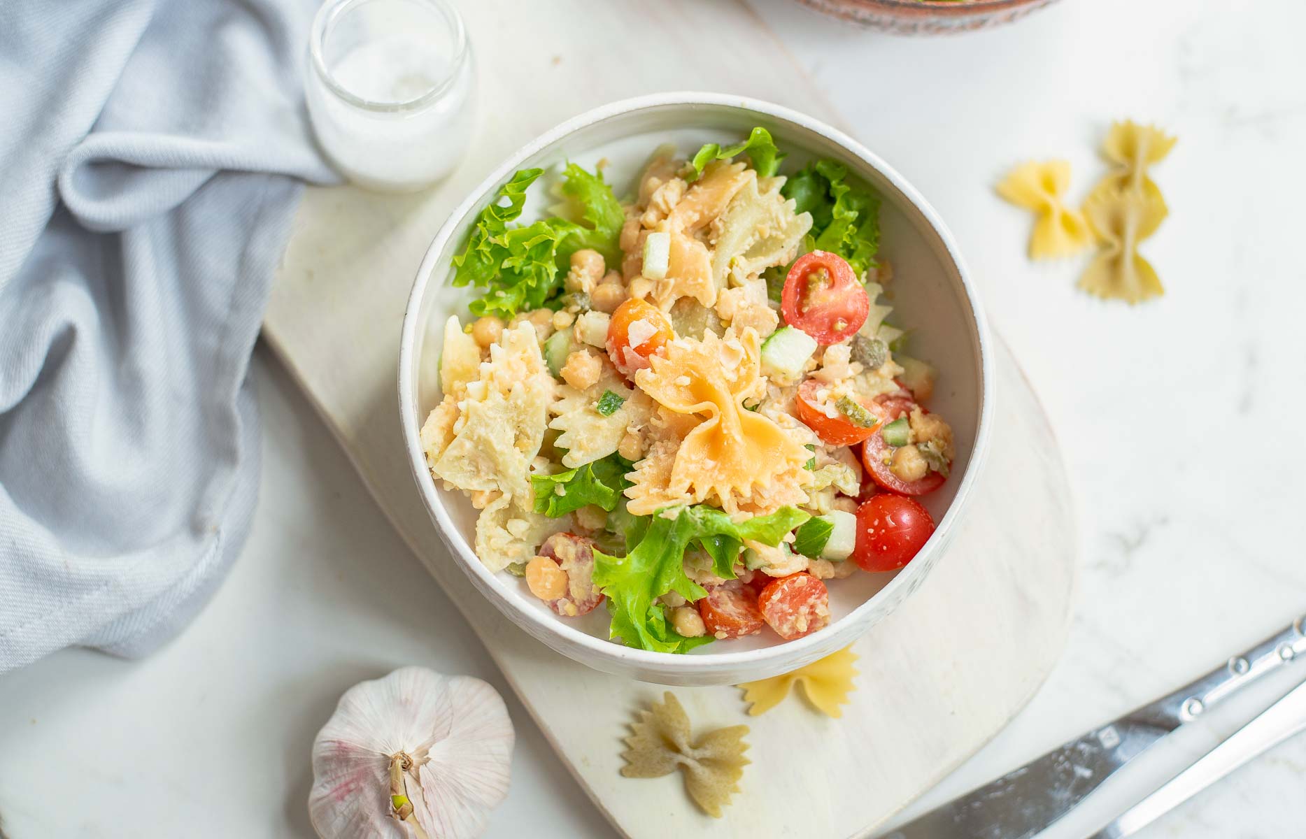 Serving of pasta salad with vegetables and beans in white bowl.
