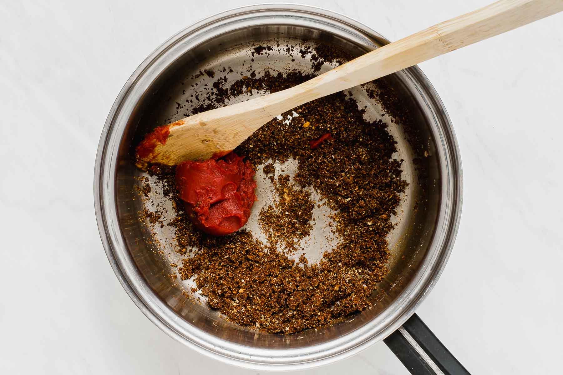 Adding tomato paste to spices sautéing in oil.