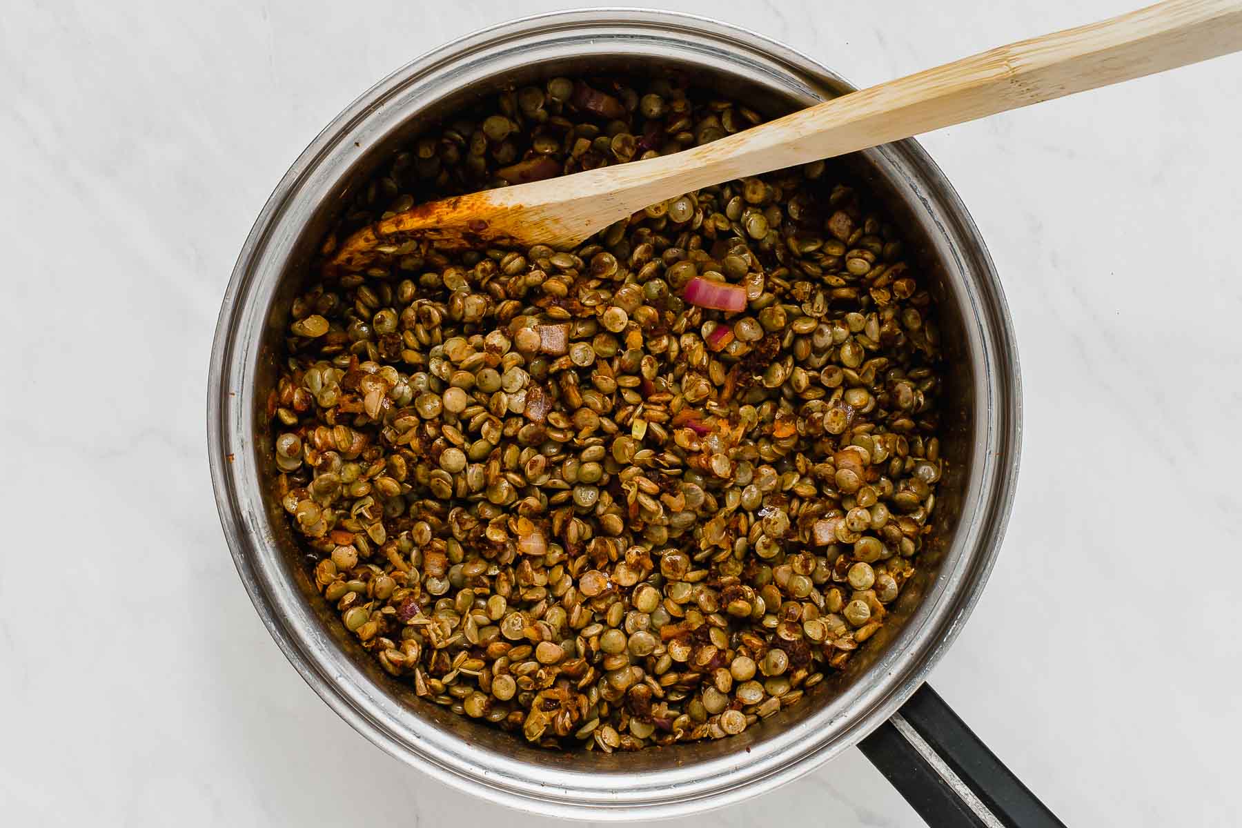 Lentils cooked in pot with wooden spoon.