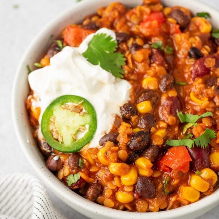 Close up of bowl of lentil and bean chili with sour cream and jalapeno slice on top.