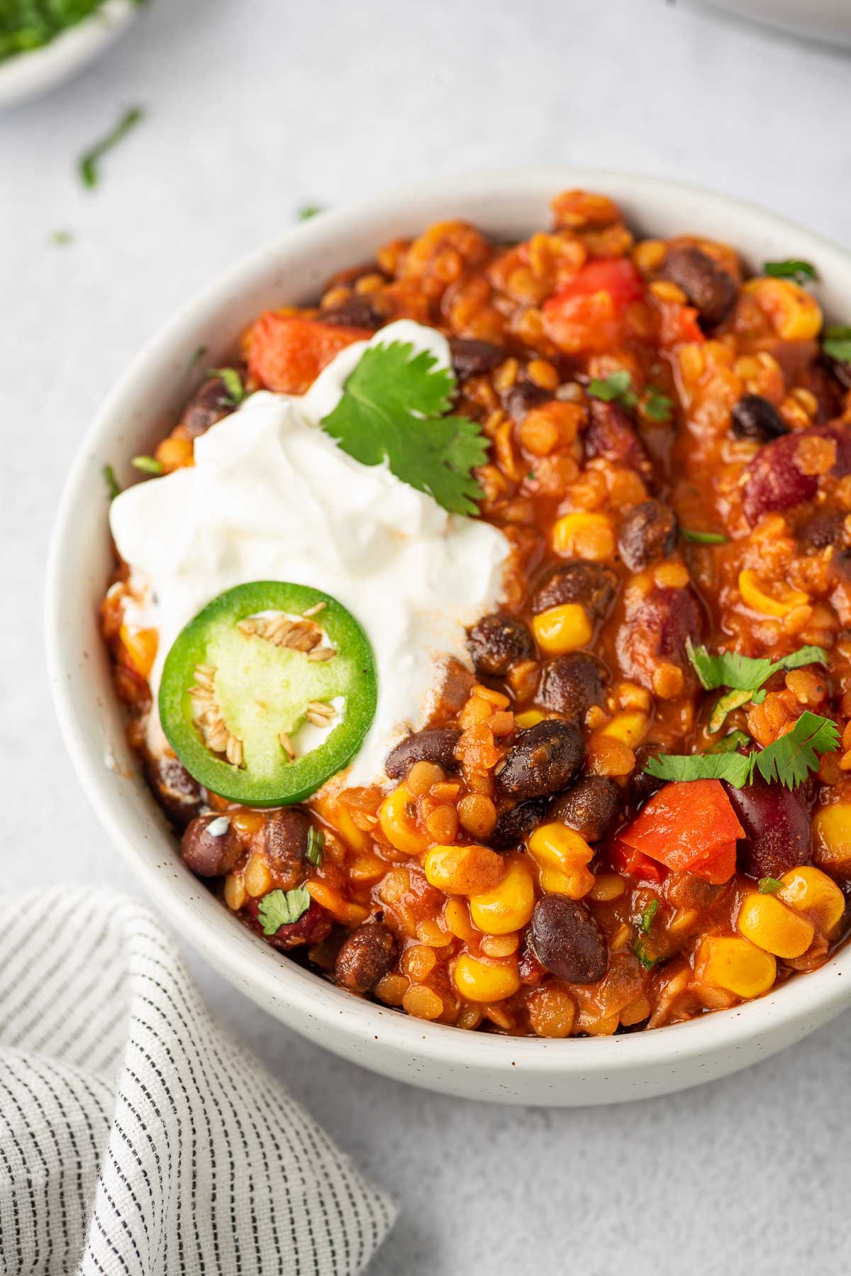 Close up of bowl of lentil and bean chili with sour cream and jalapeno slice on top.