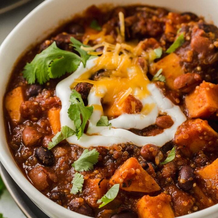 Bowl of sweet potato and black bean chili with quinoa garnished with sour cream and cheese.