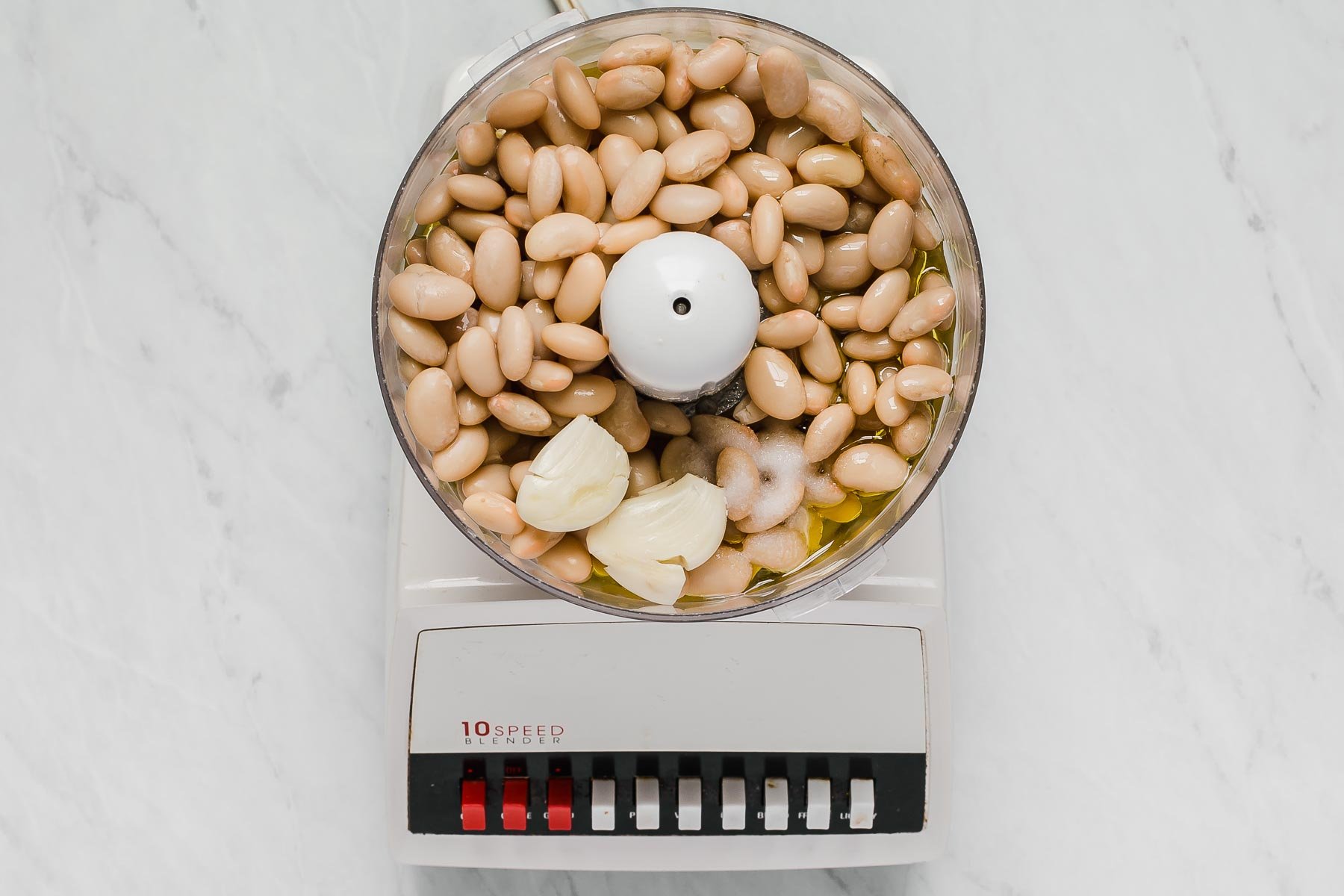 White beans and garlic cloves in the bowl of a food processor.