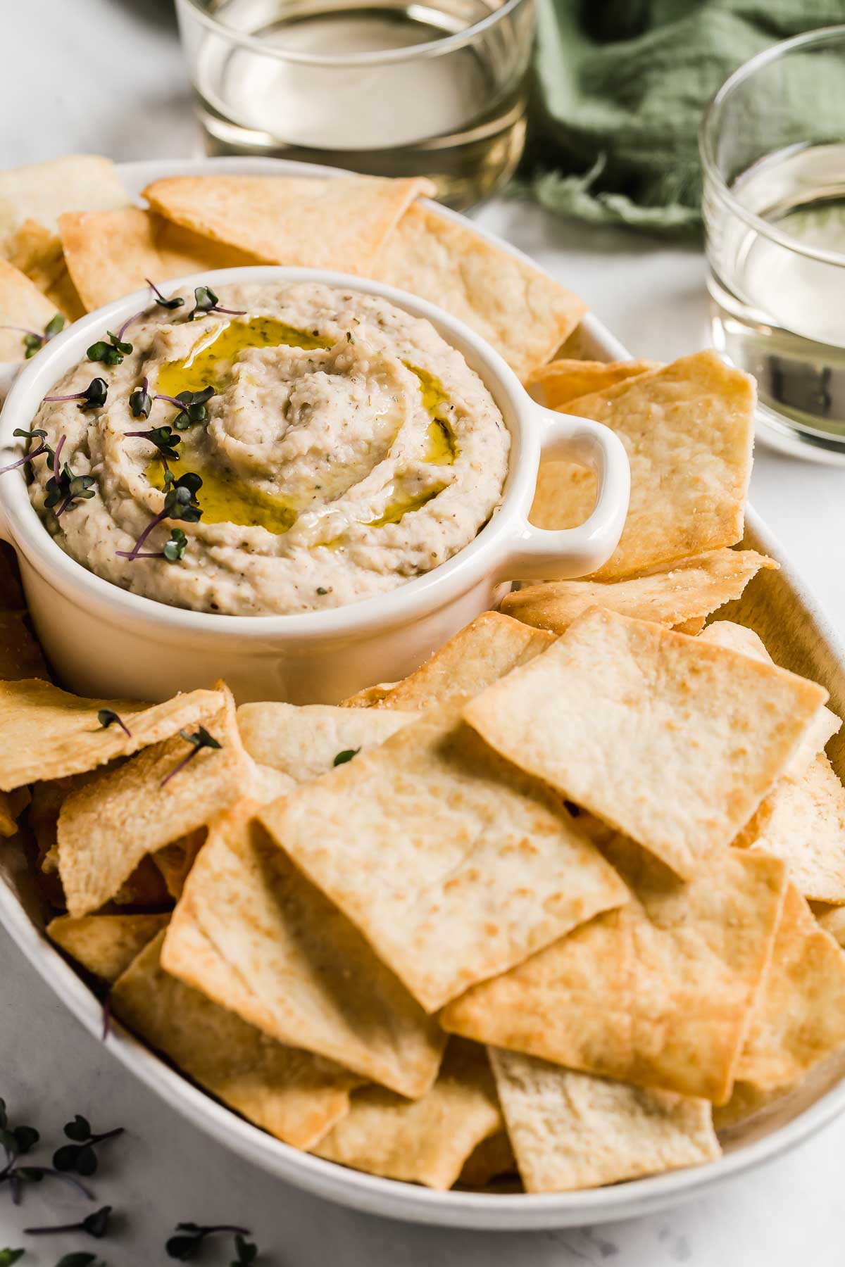 White bean dip in small cup with pita chips around it.