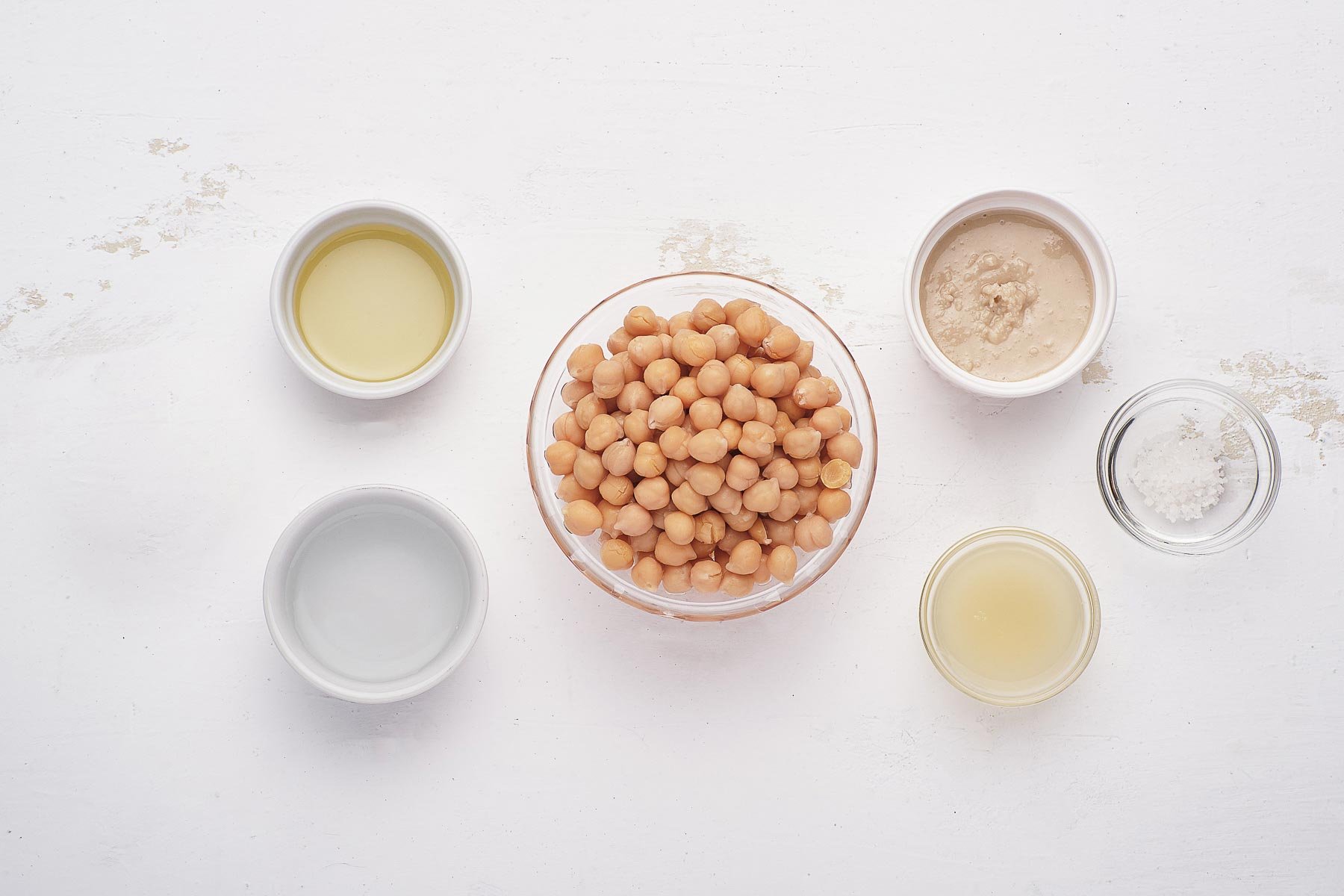 Beans, tahini, and lemon juice in small bowls on white table.