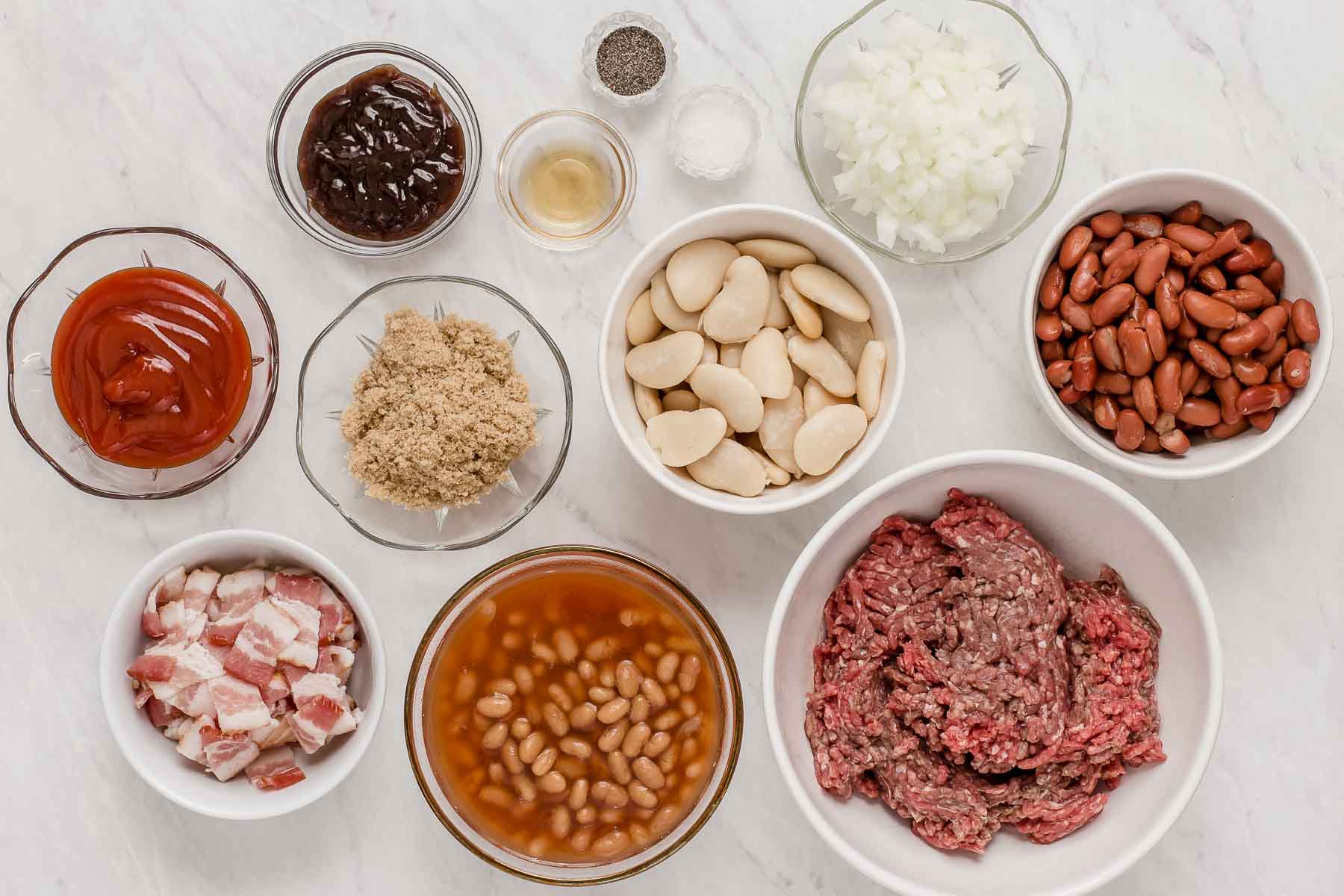 Ingredients for crockpot calico beans in small bowls on white table.