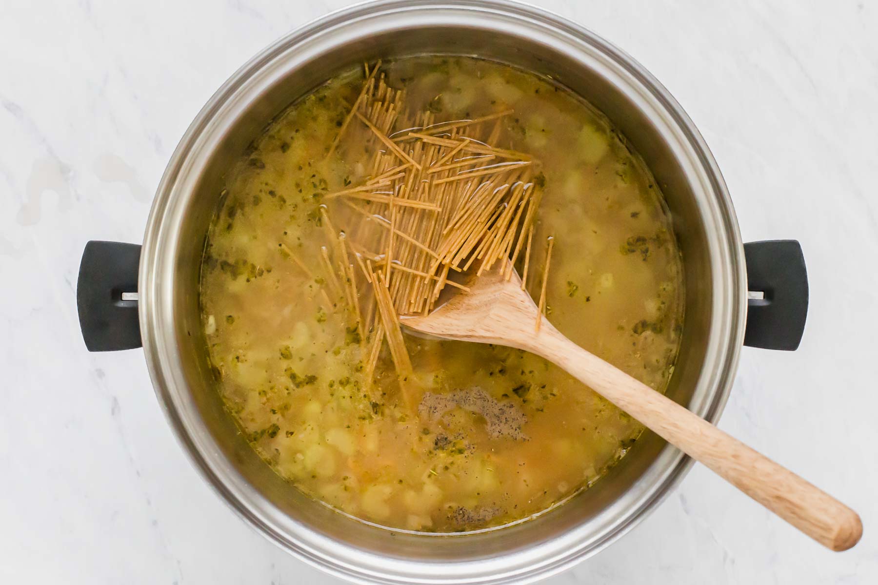 Adding broken spaghetti noodles to soup pot.
