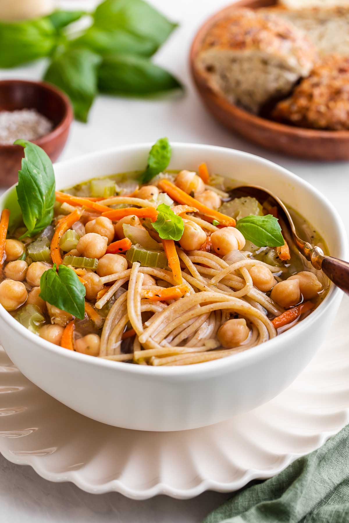 A bowl of noodle soup with chickpeas, grated carrots and fresh basil leaves.