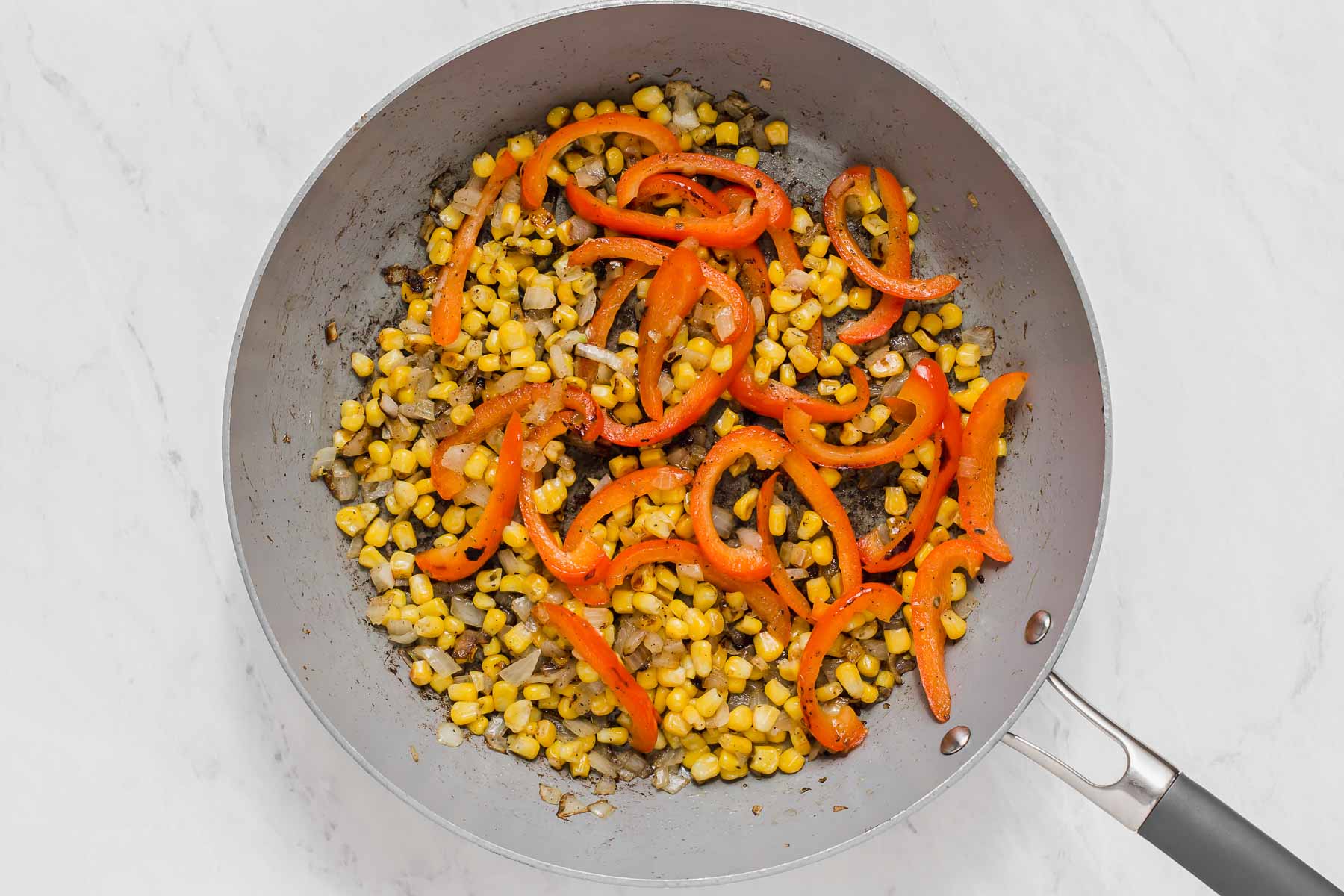 Corn, peppers and onions searing in a grey skillet.