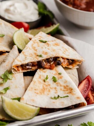 Black bean quesadillas on a sheet pan with lime and tomatoes.