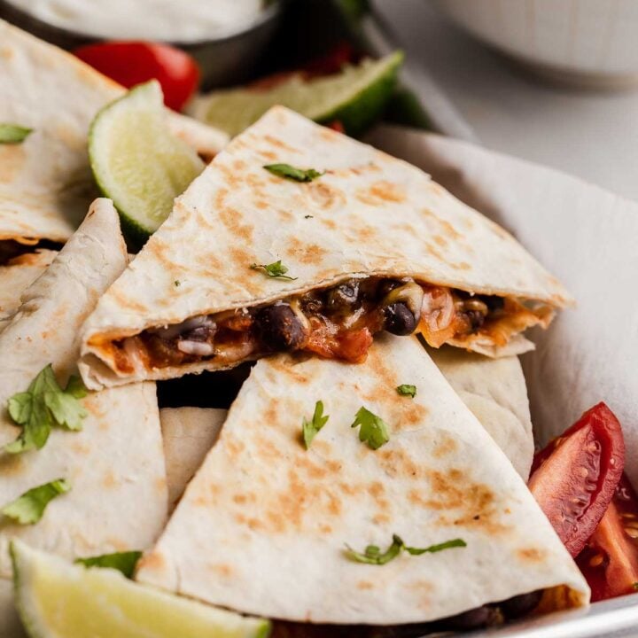 Black bean quesadillas on a sheet pan with lime and tomatoes.