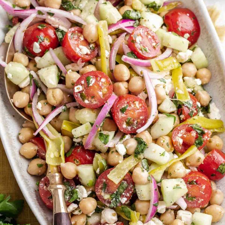 Tossed Mediterranean chickpea salad on oval serving platter with tongs.