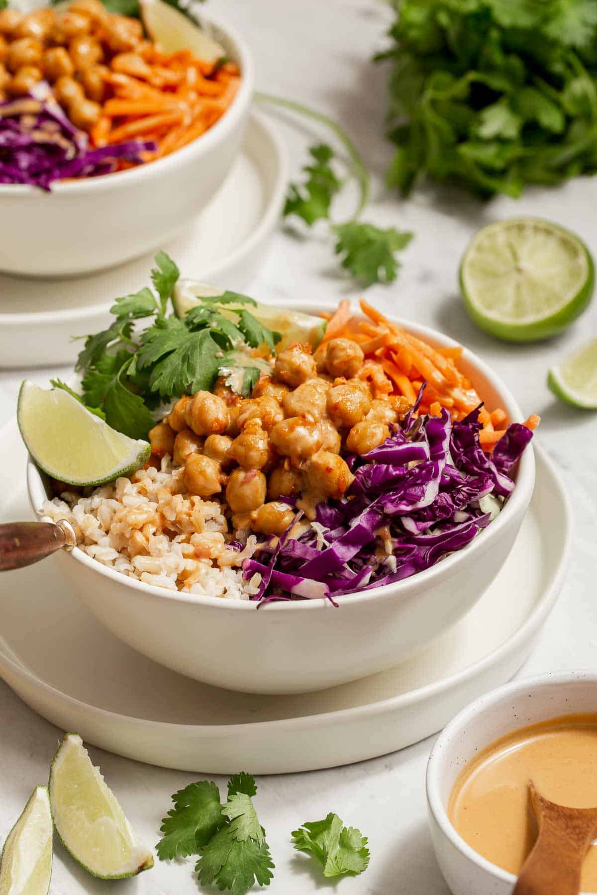 White bowl with chickpeas, purple cabbage, cilantro, carrots and lime wedge.