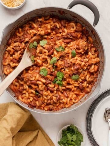 Grey skillet with chili mac recipe with kidney beans and wooden spoon.