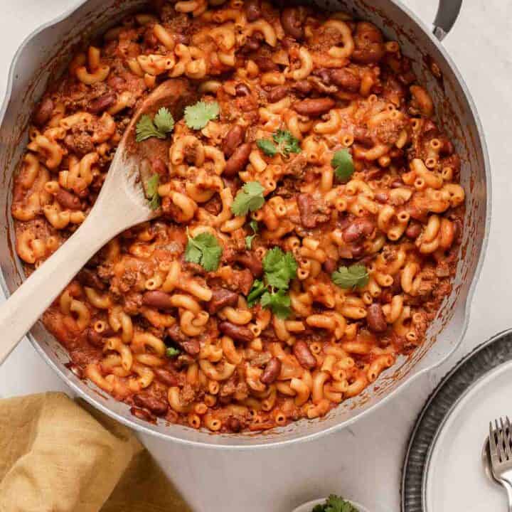 Grey skillet with chili mac recipe with kidney beans and wooden spoon.