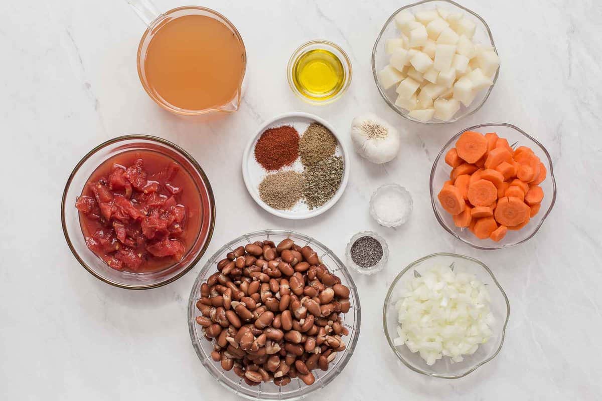 Ingredients for pinto bean soup in small bowls on white counter.