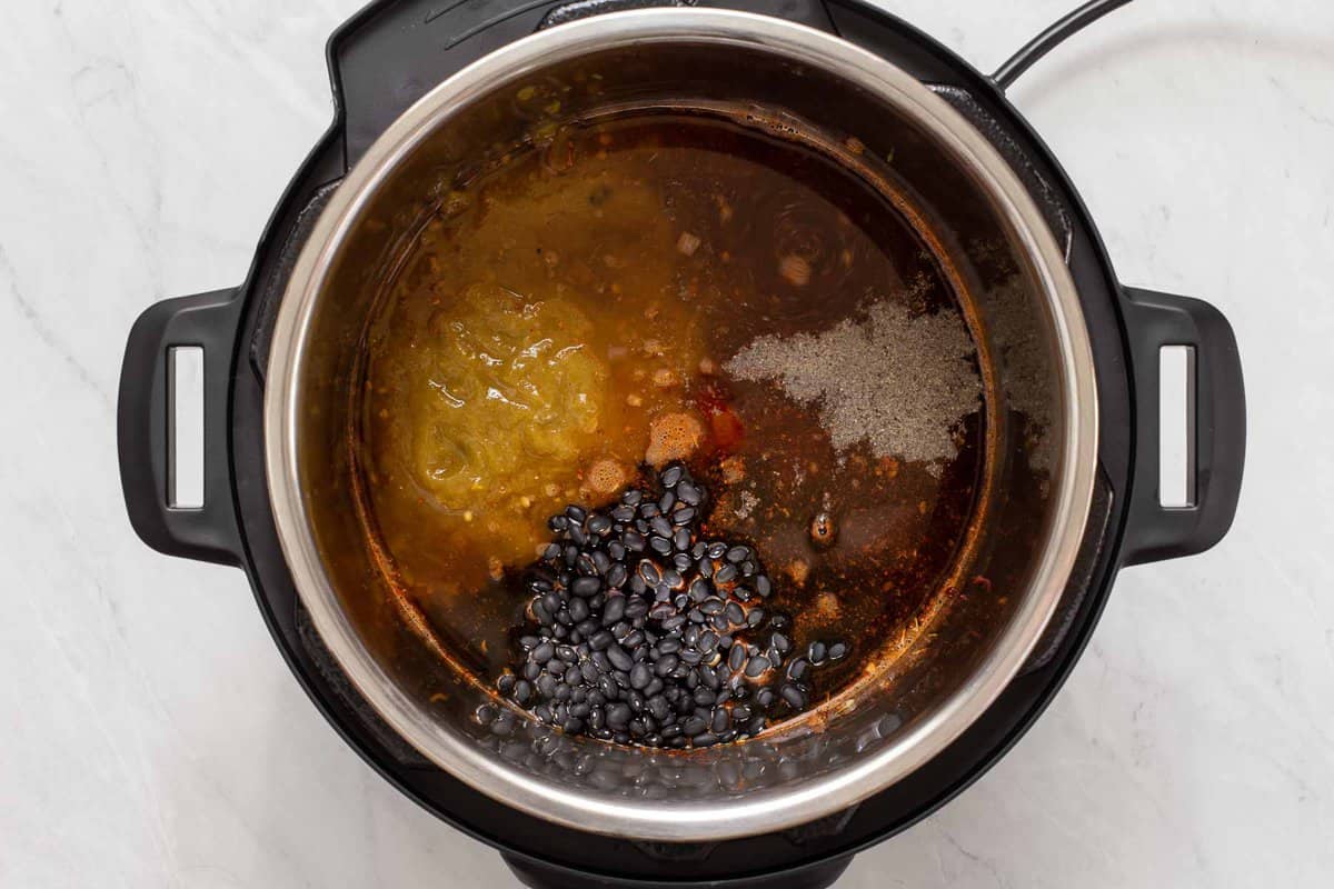 Adding dry black beans, salsa, broth and salt and pepper to instant pot black bean chili.