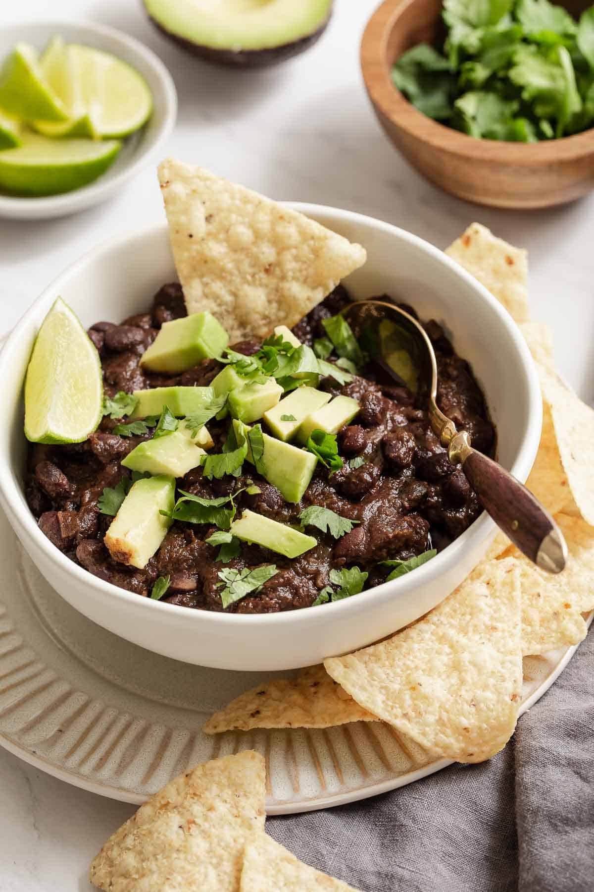 White bowl of instant pot black bean chili garnished with avocado and chips.