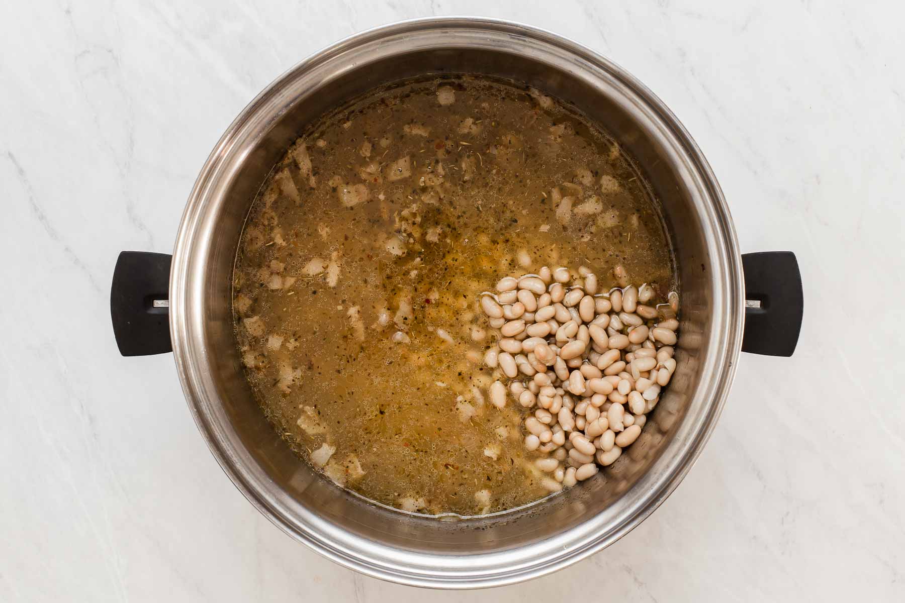 White beans in a soup pot full of chicken broth, onions and spices.