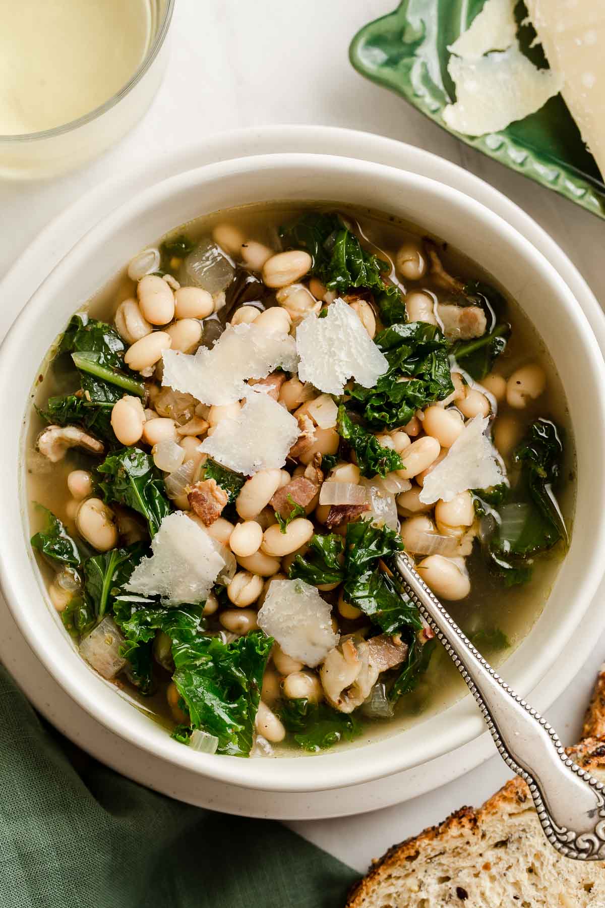 White bean kale soup with Parmesan curls on top in white bowl.