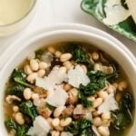 Pin image close up of white bean kale soup with spoon in white bowl.