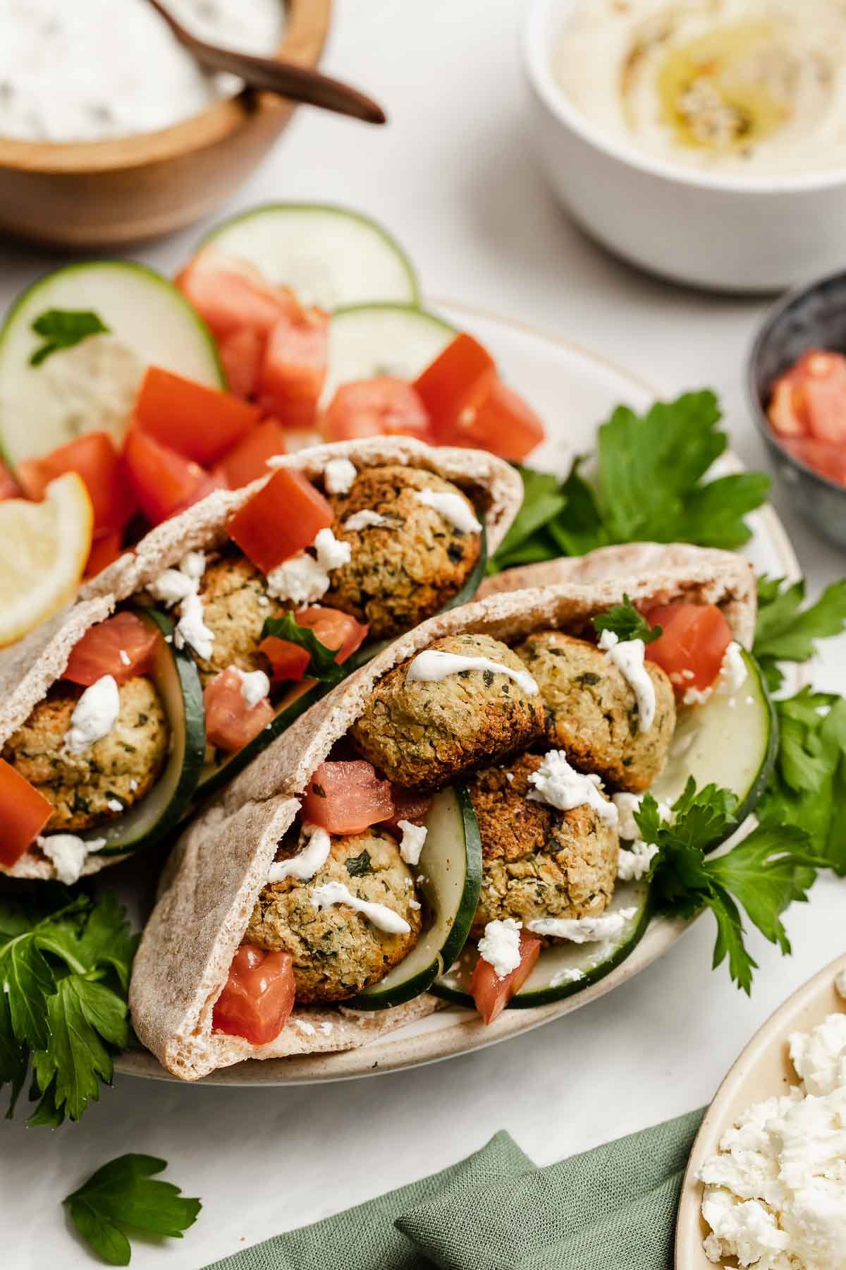 Pitas, split open and stuffed with baked falafel, cucumbers, tomatoes and drizzled with white sauce.