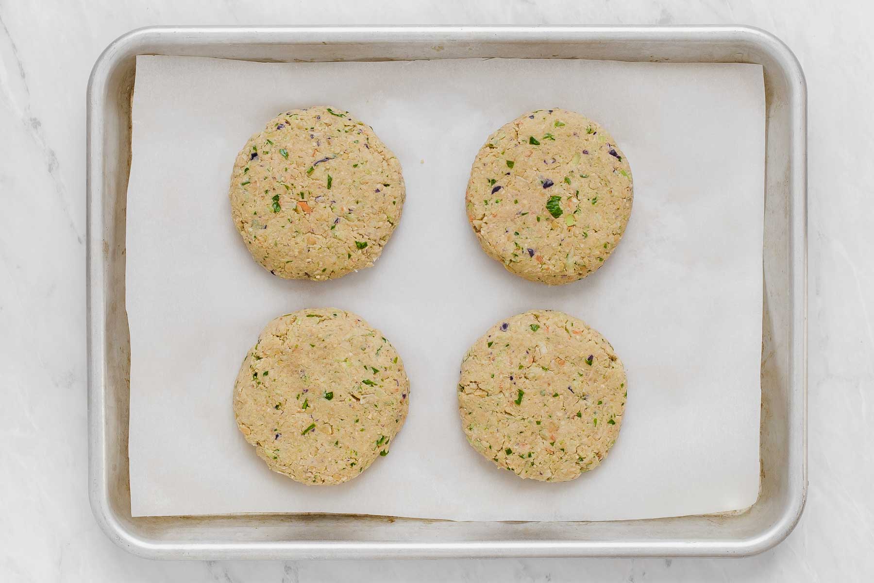 Pureed chickpeas with vegetables shaped into four patties and resting on parchment lined sheet.