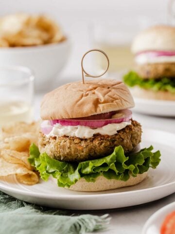 Vertical image of chickpea burgers on bun with lettuce, mayo and a slice of tomato.